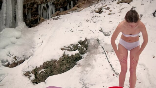 A naked woman in winter is doused with ice water from a bucket