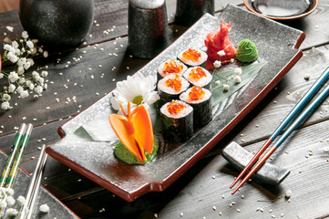 Sushi rolls with salmon and hot tea ceremony on black wooden table