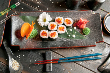 Sushi rolls with salmon and hot tea ceremony on black wooden table