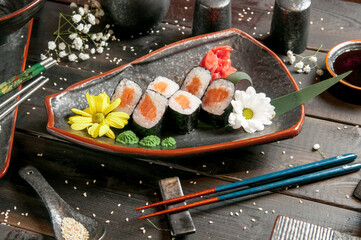 Sushi rolls with salmon and hot tea ceremony on black wooden table