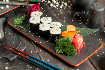 Sushi rolls with salmon and hot tea ceremony on black wooden table
