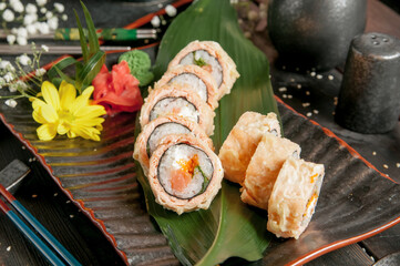 Sushi rolls with salmon and hot tea ceremony on black wooden table
