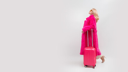 blonde woman on a white background in a pink fur coat with a pink suitcase going on a trip