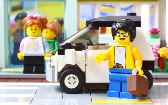 Lego minifigure of business lady is standing in front of car. Editorial illustrative image of season sales in the city. Studio shot.