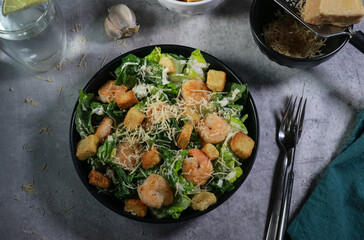 Cesar salad with grilled shrimp, croutons and parmesan cheese on grey marble table 