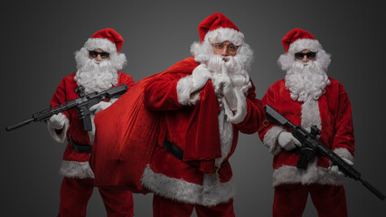 Shot of santa carrying bag with christmas presents around two santa with rifles.
