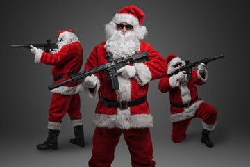 Studio shot of stylish crew of three santa with rifles isolated on grey background.