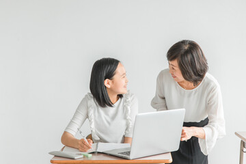 学校の教室でノートパソコンを使いながら勉強する女子小学生と女性講師（教育・先生・授業・家庭教師）
