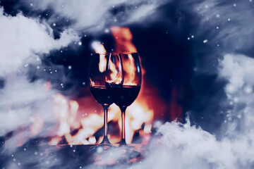 Winter atmosphere and Christmas holiday time, wine glasses in front of fireplace covered with snowy effect on window glass, holidays backgrounds