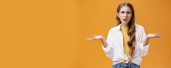 What, I do not understand. Portrait of arrogant questioned impolite girl being pissed with questiones shrugging with hands spread sideways making irritated grimace standing confused over orange wall - obrazy, fototapety, plakaty