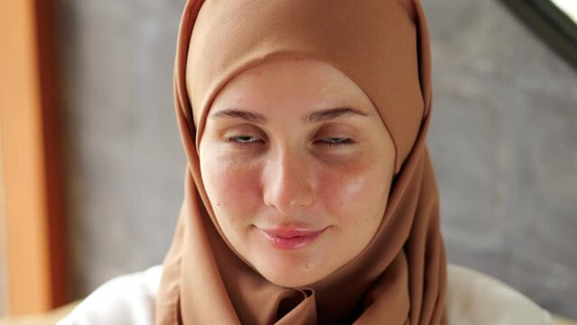 Young woman with hair and head covered in hijab slightly turns her head and looks directly into the camera with humble smile. Close portrait shot, positive attitude from lady