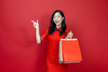 Fototapeta na wymiar Asian chinese woman with red cheongsam or qipao holding shopping bag wish the good luck sale and prosperity in Chinese New Year celebration holiday isolated on red background