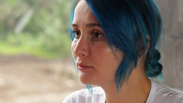 A Young Woman Crying, Close-up Portrait, Tears And Tear-stained Mascara Can Be Seen On Her Cheeks. She Look Aside, Blurred Green Outdoors And Room Wall On Background