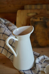 Rustic kitchen items. Enameled metal white jug for milk or water on the kitchen table in a log house