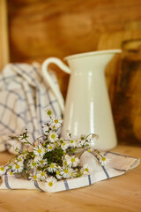 Rustic kitchen items. Enameled metal white jug for milk or water and a bouquet of wildflowers on the kitchen table in a log house