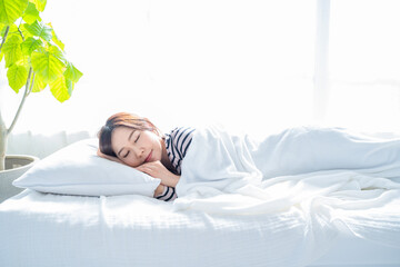 明るいシンプルな部屋のベッドで眠る女性