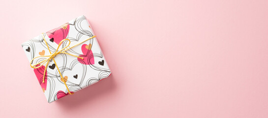 Valentine's Day concept. Top view photo of giftbox in wrapping paper with heart pattern on isolated pastel pink background with empty space