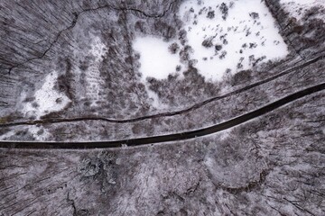 Aerial view of a road in forest covered in snow, in a mountainous rural area, from Romania. Captured with a drone, in winter conditions.
