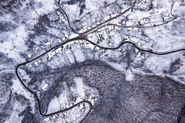 Aerial view of a village covered in snow, in a mountainous rural area, from Romania. Captured with a drone, in winter conditions.
