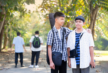 asian school boy carrying a guitar bag are walking to learn music, teenage friends having fun and talking together