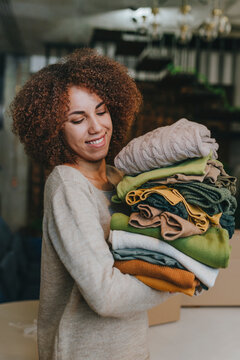 Happy young fashion designer standing with clothes in workshop