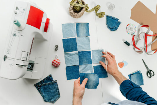 Hands of fashion designer working on pieces of denim on table