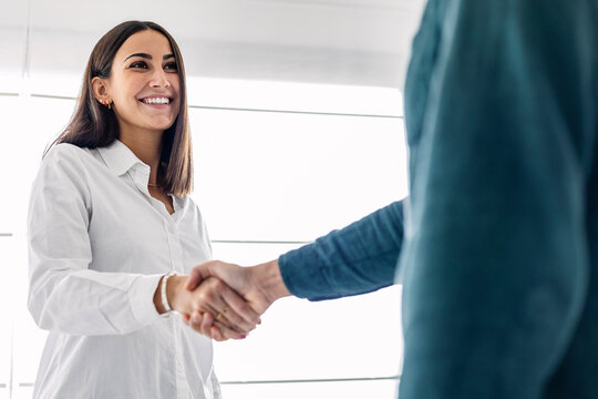 Happy young businesswoman shaking hand with colleague at workplace