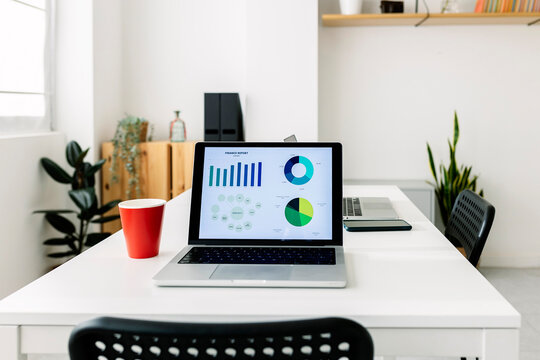 Bar graph and pie chart on laptop screen by coffee cup at office