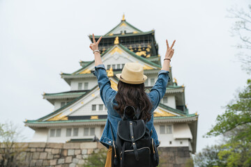 rear view of funny Asian female traveler showing peace sign with two hands while taking picture...