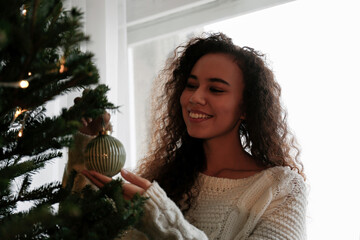 Happy young woman decorating Christmas tree with bauble at home