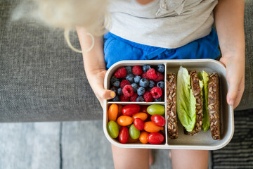 Hands of girl holding lunch box with healthy food on sofa at home