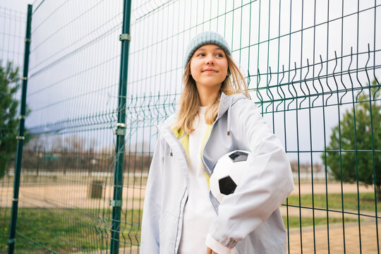 Contemplative girl wearing knit hat standing with soccer ball