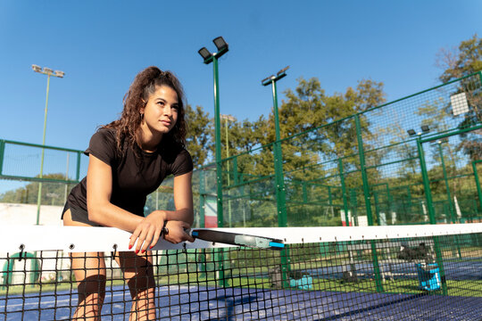 Young woman with racket leaning on tennis net