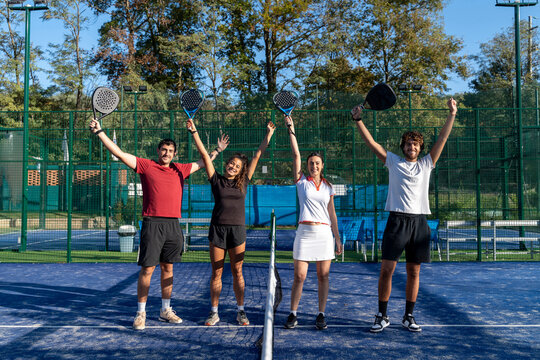 Happy men and women with arms raised standing at sports court - Powered by Adobe