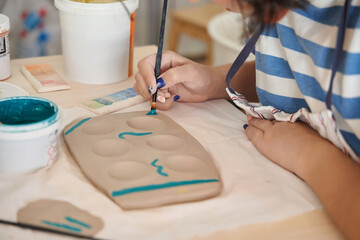 Woman painting and decorating a pottery in a ceramic workshop. Craft, art and hobbies concept.