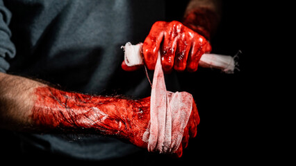 A man covered in blood bandages his hands.