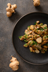 Fototapeta premium Roasted Jerusalem artichoke root, topinambur, sunchokes with garlic and parsley on brown background. Top view. Vertical format.