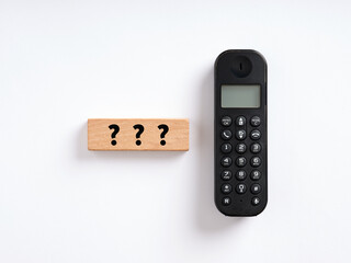 Customer help and support concept. Question marks on wooden block with a wireless phone.