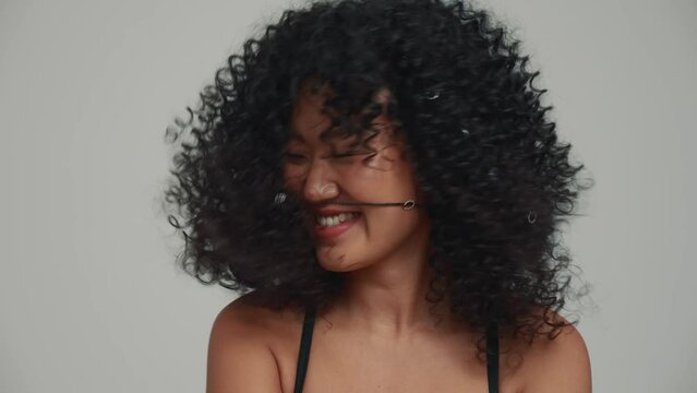 Portrait of funny brunette Asian woman shaking her head at the camera in the grey studio