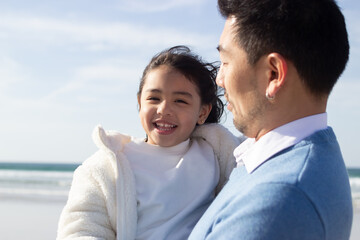 Smiling little girl in white coat on beach. Japanese child on beach on summer day. Father holding child. Childhood, portrait, happiness concept