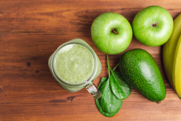 Green smoothie drink blended in a glass jar, avocado, spinach leaves, banana and apples at wooden...