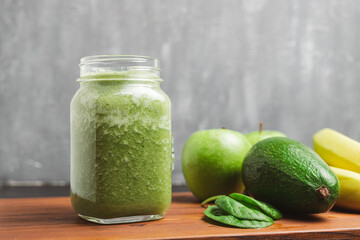 Green smoothie drink blended in a glass jar, avocado, spinach leaves, banana and apples at wooden board