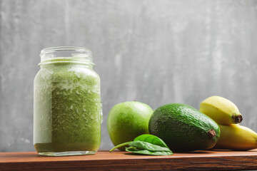 Green smoothie drink blended in a glass jar, avocado, spinach leaves, banana and apples at wooden...