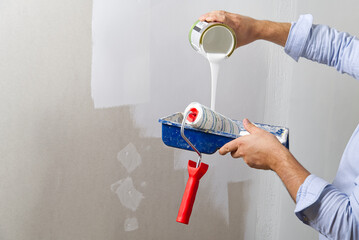 Men hand painting wall with paint roller with white color. Painting apartment, renovating with white color paint - Powered by Adobe
