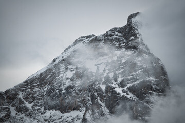 Dreamy mysterious winter landscape with fog and snow covered mountains and clouds in the sky