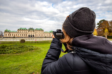 Young girl with camera is taking a photo at Schloss Belvedere in Vienna. Beautiful girl traveling in winter in Vienna. - 556648452