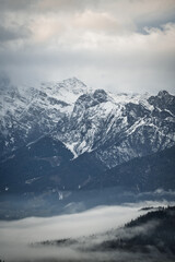 Fototapeta na wymiar Dreamy mysterious winter landscape with fog and snow covered mountains and clouds in the sky