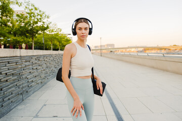 Fototapeta premium Young sportswoman listening to music while walking along embankment