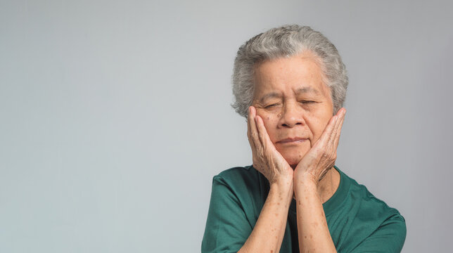 Senior Woman With Short Gray Hair Suffering From A Toothache While Standing On A Gray Background