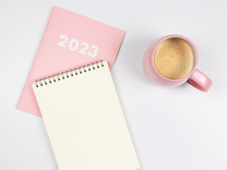  blank paper note book on pink diary 2023 and pink cup of coffee on white background.